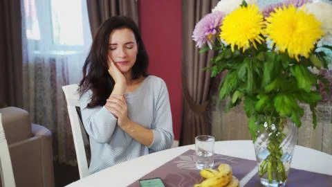 A sharp toothache from cold water in a brunette girl at the table at home. Stock Photos