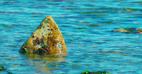Sharp triangular stone emerges from rippling blue sea water 库存影片 334327055