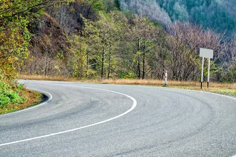 A sharp turn on the road between green trees and small mountains. Stock Photos