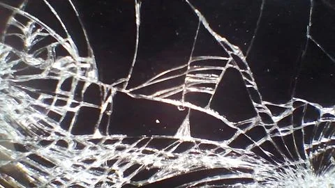 Sharp white cracks spread across a dark shattered glass surface Foto stock