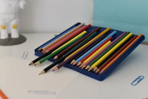 Sharpened colored pencils organized in blue plastic case on white desk surface Foto stock
