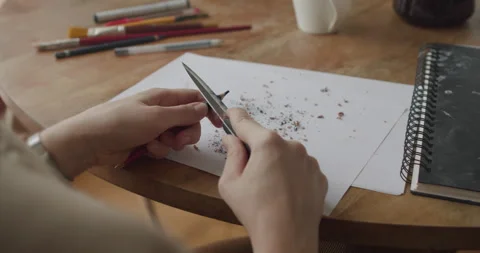 Sharpening a black pencil using a knife on a wooden table. Artistic workspace Stock Footage 301617271