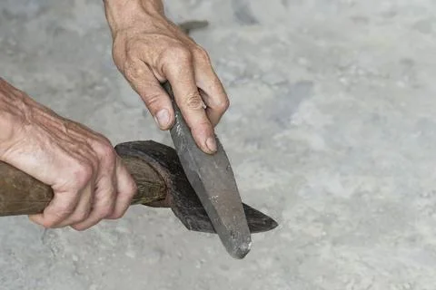 Sharpening the blade of an axe. A man sharpens the blade of an old rusty axe  Stock Photos