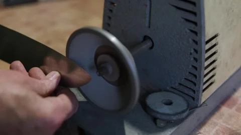 Sharpening a kitchen knife on an electric grinder in a home workshop. DIY Stock Footage 323438061