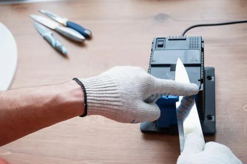 Sharpening a knife on an electric sharpener at home. The man's hand drives .. Foto stock