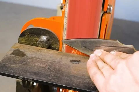 Sharpening throwing knife on a grinding machine. Stock Photos
