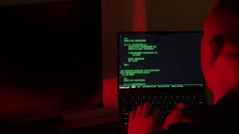 Shaved head person types on laptop with green code under shifting blue purple Stock Footage 345521327