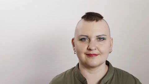 A shaved woman with a mohawk smiles class at the camera on a gray background 库存影片 201201874