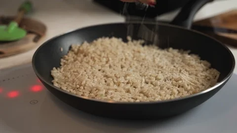 Shaving bits of parmesan cheese into hot risotto in a large stainless steel pan Video stock 99470953