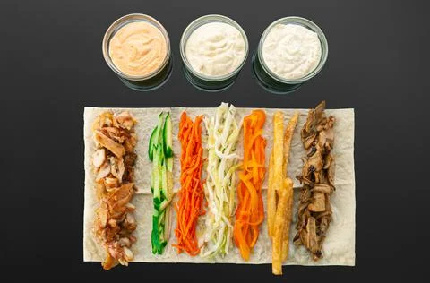 Shawarma ingredients. On a thin flat cake: grilled meat, cucumber, carrots, c Stock Photos