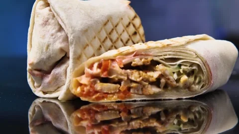 Shawarma split in two on a black mirrored surface. Camera rotates around Stock Footage 244700995