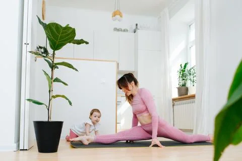 She doing exercises dropping into the splits, next to crawls her little daugh Stock Photos
