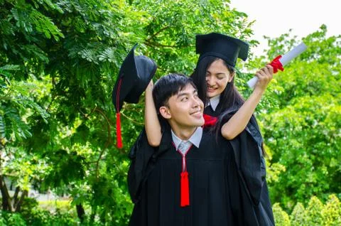 She is hugging him from the back is smiling and holding hat with park background Stock Photos
