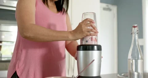 She is placing cup on base, starting blender and holding cup, making pink Stock Footage 336658434