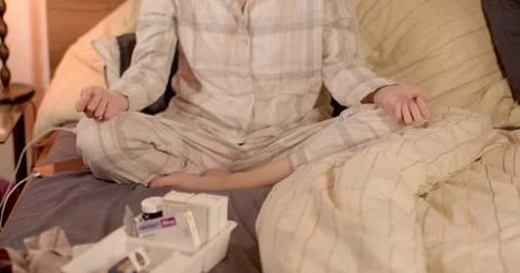 She is sitting on the bed with her legs folded. Bed yoga. Stock Photos