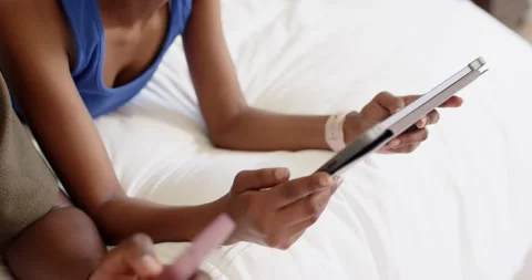 She is tapping tablet, he is scrolling pink phone, camera panning left, both Stock Footage 344949066