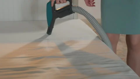 She vacuums bed with device. Maid uses handheld tool on bedding fabric. Person Stock Footage 345516442