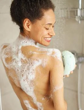 She washes her barechested back with a sponge in the shower, smiling Stock Photos