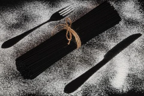 Sheaf of black spaghetti on background with fork and knife silhouette made wi Stock Photos