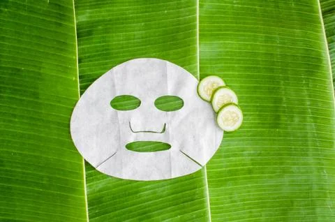 Sheet face mask with cucumber on the background of banana leaf. Stock Photos