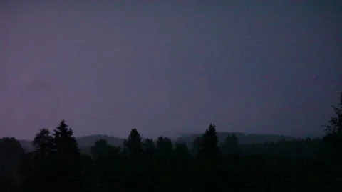 Sheet lightning during a dark summer night illuminates a wooded landscape Stock Footage
