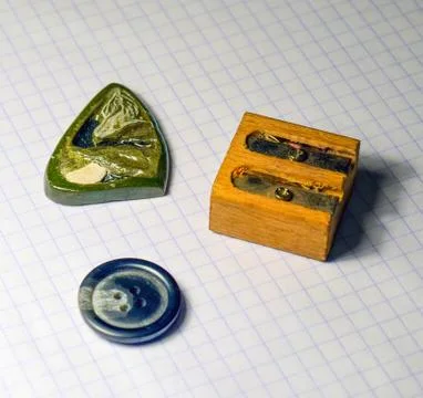 On a sheet of notebook pencil sharpener, a button and a stone amulet Stock Photos