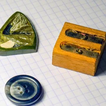 On a sheet of notebook pencil sharpener, a button and a stone amulet Stock Photos