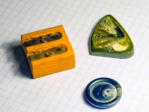 On a sheet of notebook pencil sharpener, a button and a stone amulet Stock Photos