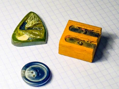 On a sheet of notebook pencil sharpener, a button and a stone amulet Stock Photos