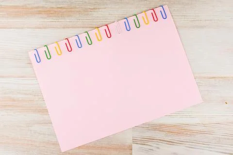 A sheet of pink paper fixed with multi-colored paper clips on a light Board t Stock Photos