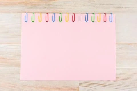 A sheet of pink paper fixed with multi-colored paper clips on a light Board t Stock Photos