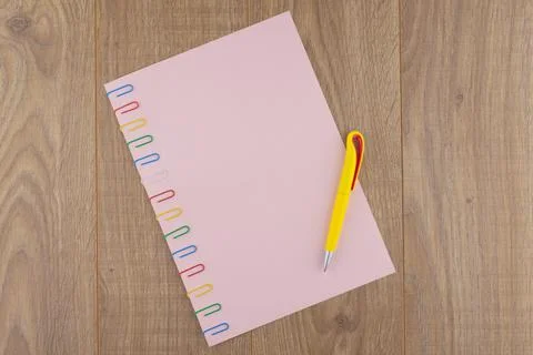 A sheet of pink paper fixed with multi-colored paper clips on the oak plank t Stock Photos