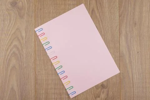 A sheet of pink paper fixed with multi-colored paper clips on an oak plank ta Stock Photos