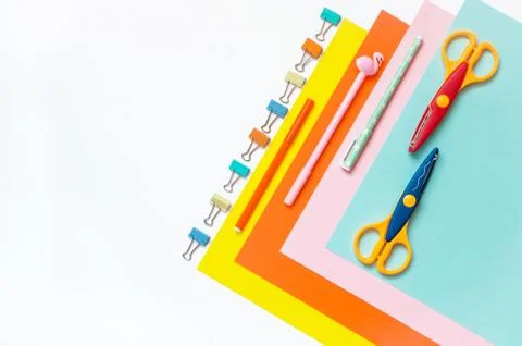 Sheets of colored paper, scissors and supplies on a white table. Stock Photos