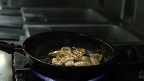 Сhef in the kitchen prepares shrimp on a hot pan sprinkling them with spices Video stock 103310509