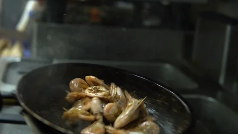 Сhef in the kitchen prepares shrimp on a hot pan sprinkling them with spices Video stock 103310537
