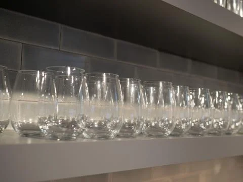Shelf with multiple rows of small wine glasses in kitchen Stock Photos