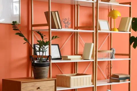 Shelf unit with books and frames near orange wall in room Фото
