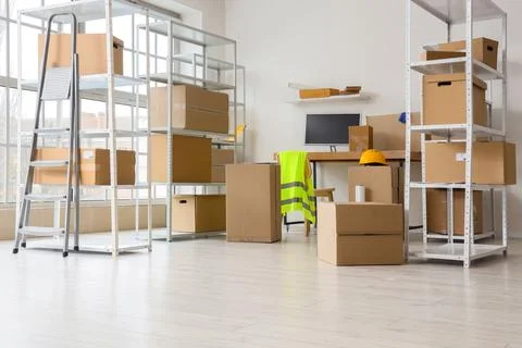 Shelf units with cardboard boxes and workplace in warehouse Stock Photos
