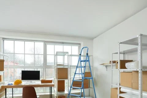 Shelf units with cardboard boxes, workplace and stepladder in warehouse Stock Photos