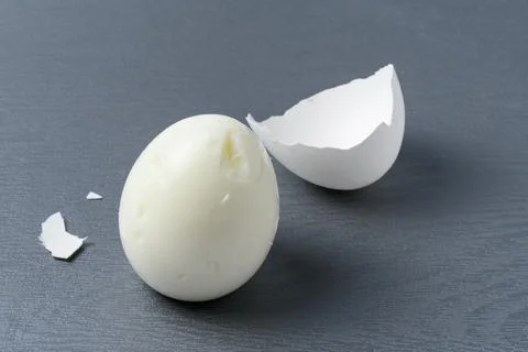 Shell and peeled hard-boiled egg on gray textured background Stock Photos