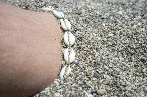 Shell ankle bracelet on half buried male leg Stock Photos