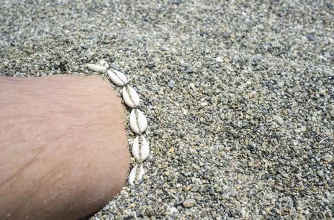 Shell ankle bracelet on half buried male leg Stock Photos