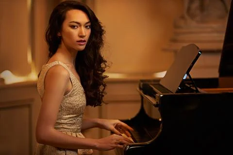 Shell be entertaining you tonight. a beautiful young woman playing the piano in Stock Photos