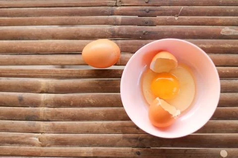 Shell with egg and open Eggs in a pink bowl on Bamboo battens. Top view close Stock Photos