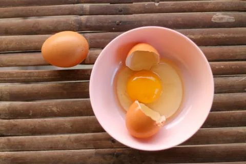 Shell with egg and open Eggs in a pink bowl on Bamboo battens. Top view close Stock Photos