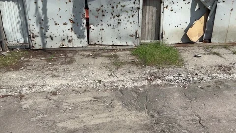 A shell explosion crater on the road and on the garage door. War in Ukraine. 스톡 동영상 236122853
