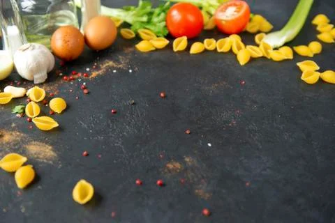 Shell shaped pasta, eggs, spices, tomato, celery, garlic on black background Stock Photos