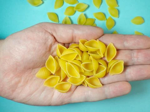 Shell-shaped pasta falls from your hand. Italian food. Cuisine of the peoples Stock Photos