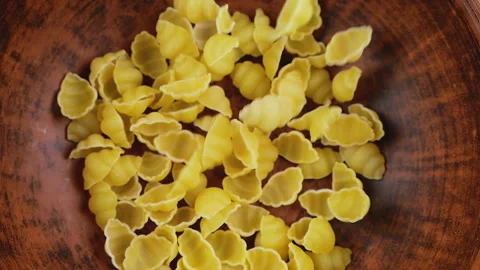 Shell-shaped pasta is poured into a brown ceramic bowl. Top view. Slow motion. Stock-Footage 304386146